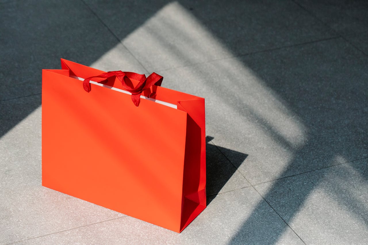 Bright red paper bag on pavement surface under sunlight, ideal for shopping concepts.